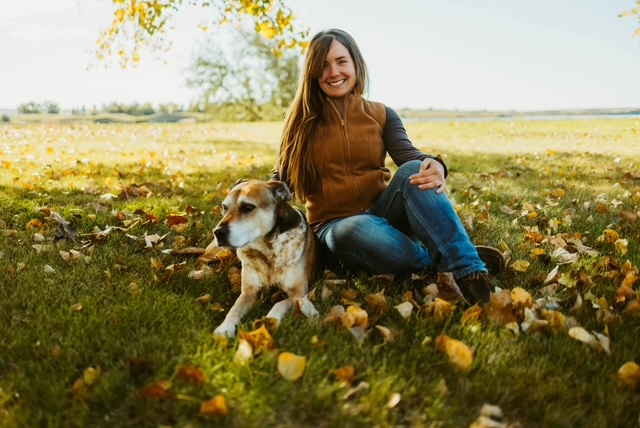A woman sitting on autumn leaves with her dog in a sunny park.