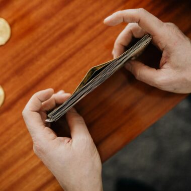 Close-up of hands counting currency with coins scattered on a wooden table. Perfect for finance and business themes.